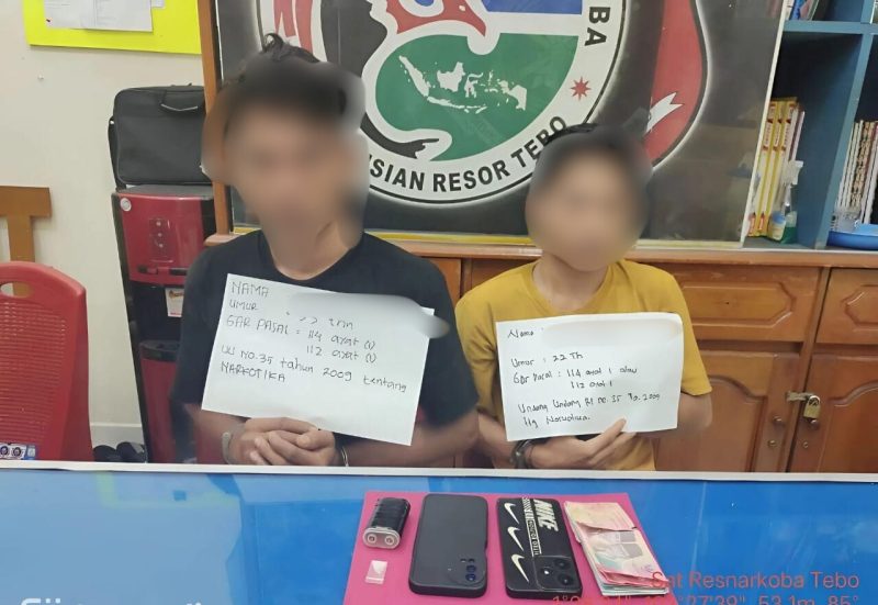 Dua tersangka kasus penyalahgunaan narkotika jenis sabu yang diamankan oleh Satresnarkoba Polres Tebo. Tampak keduanya memegang papan identitas berisi data singkat dan pasal yang disangkakan, dengan barang bukti berupa satu paket sabu, dua unit handphone, uang tunai, serta alat hisap sabu turut diamankan dan diperlihatkan di meja.(INJ/Ist)