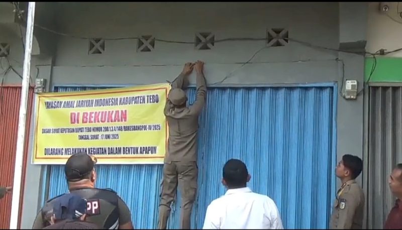 Petugas Satpol PP Kabupaten Tebo memasang spanduk penutupan di depan kantor Yayasan Amal Jariyah Indonesia (YAJI) di Kelurahan Wiroto Agung, Kecamatan Rimbo Bujang, Jumat (4/7/2025). Penutupan dilakukan berdasarkan Surat Keputusan Bupati Tebo karena yayasan diduga terafiliasi dengan jaringan NII dan tidak memiliki izin operasional yang sah.